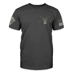 A dark grey t-shirt with two AR15's crossed over printed on the front left side of the chest.