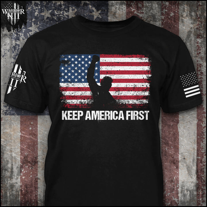 Front black t-shirt with the main design, "US Flag standing in front with his hand raised after he was shot at, with Keep America First written below" printed.