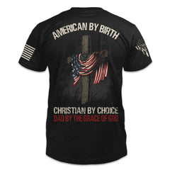 A black t-shirt featuring a design on the back of a large wooden cross with an American Flag draped over it and the words "American by Birth, Christian By Choice, Dad by the Grace of God"