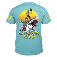 The back of a Tahiti Blue shirt with an image of a skeleton wearing American Flag shorts riding a shark, holding a short barrel rifle, in front of a setting sun with the words "Liberty or Death" underneath.
