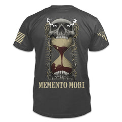 The back of an asphalt-gray t-shirt with an image on the back of an hourglass filled with red sand in the mouth of a human skull and the words "Memento Mori" underneath.