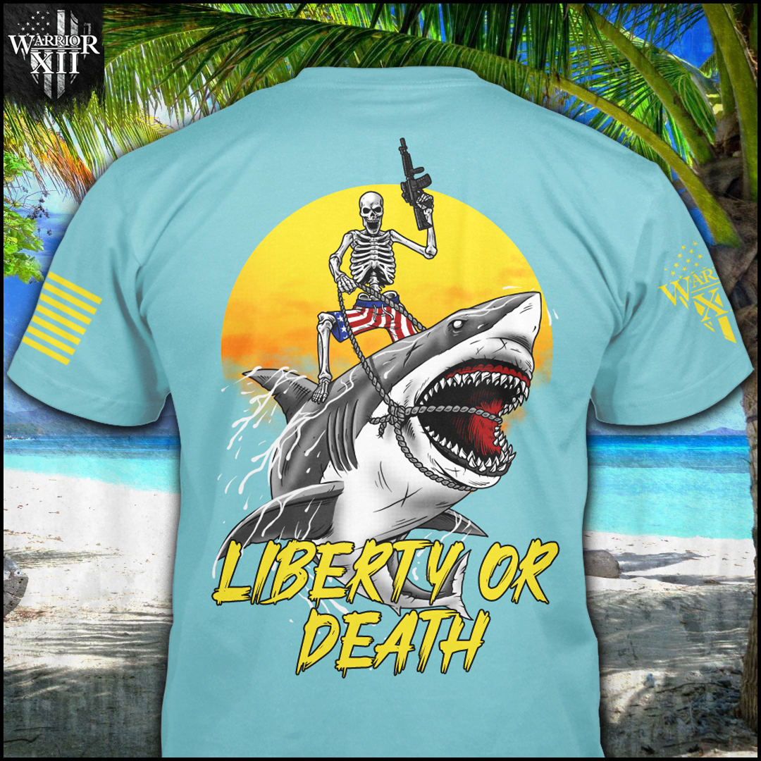 The front and back of a Tahiti Blue shirt with an image on the back of a skeleton wearing American Flag shorts riding a shark, holding a short barrel rifle, in front of a setting sun with the words "Liberty or Death" underneath.