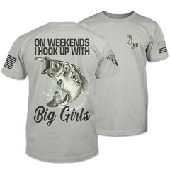 The front and back of a light grey shirt. The back features the image of a jumping largemouth bass hooked on a lure with the words "On weekends I hook up with big girls." The front features a small pocket image of a lure.
