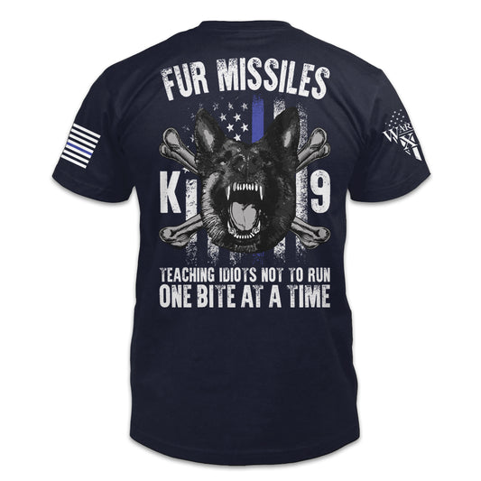 A navy blue t-shirt with the words "Fur Missiles, Teaching Idiots Not To Run, One Bite At A Time!" featuring a german shepherd showing teeth in front of a thin blue line USA flag printed on the back of the shirt.