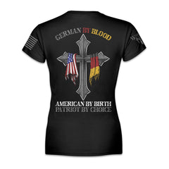 A black women's relaxed fit shirt with the words 'German by blood, American by birth, patriot by choice" and a cross with the German and USA flag hanging over it printed on the back of the shirt.