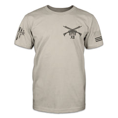 A light tan t-shirt with two guns crossed over printed on the front.