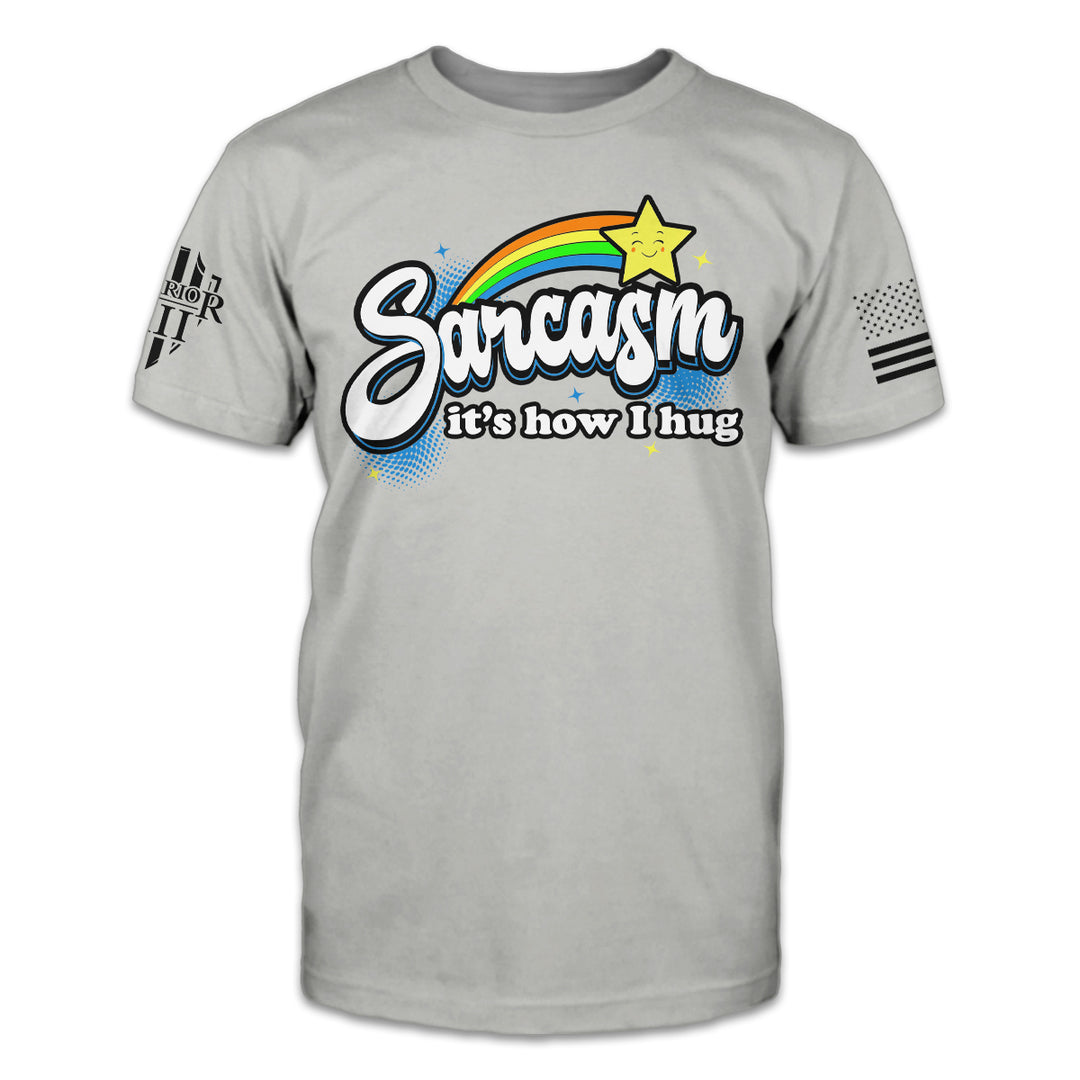 A grey t-shirt with the words "Sarcasm; it's how I hug" with a rainbow and shooting star printed on the front of the shirt.