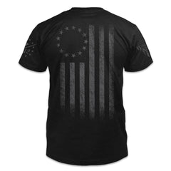 A  black t-shirt with the Tactical Betsy Ross flag shirt that pays tribute to the ideas which the United States of America was founded on printed on the back.