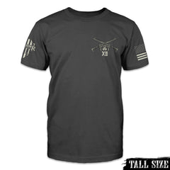 A dark grey tal size shirt with two AR15's crossed over printed on the front left side of the chest.