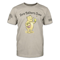 A tan t-shirt with an image of Winnie the Pooh on the front, holding a pot of honey under her right are and holding up his left hand covered in honey, with the words "Zero Bothers Given"