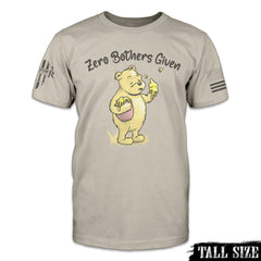 A tan t-shirt with an image of Winnie the Pooh on the front, holding a pot of honey under her right are and holding up his left hand covered in honey, with the words "Zero Bothers Given"